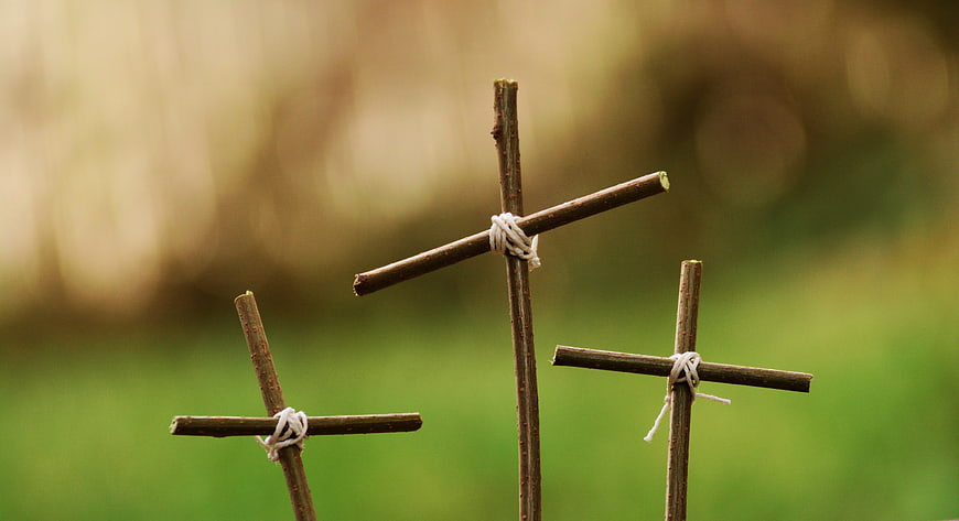Three rustic wooden crosses tied with string on blurred green background