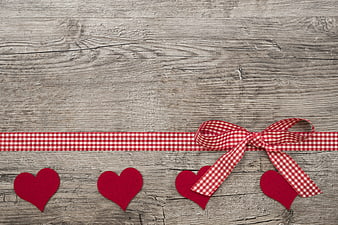 Red gingham ribbon and felt hearts on rustic wood background