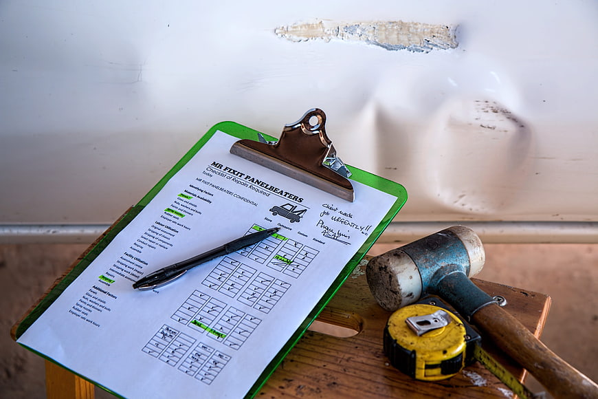 Auto body repair checklist and tools on dented car panel