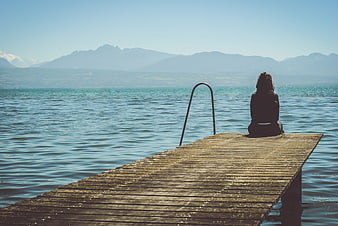 Woman sitting alone on wooden dock overlooking lake and mountains