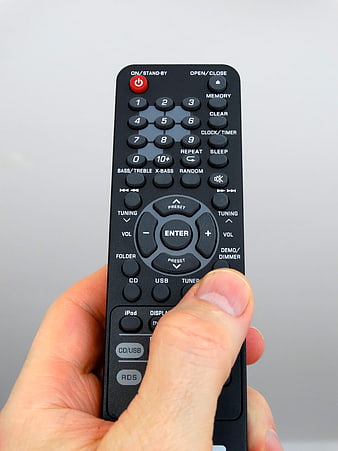 Hand holding black remote control against white background