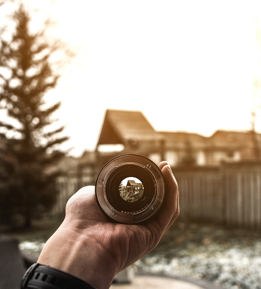Hand holding camera lens reflecting house in backyard