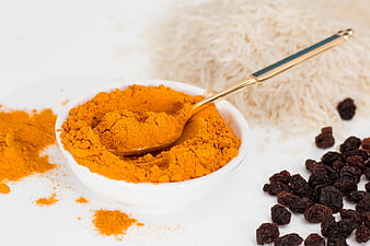 Turmeric powder, rice, and raisins on white background