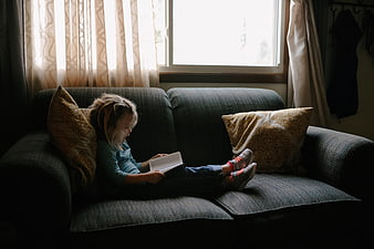 Young girl reading a book on a couch by a window