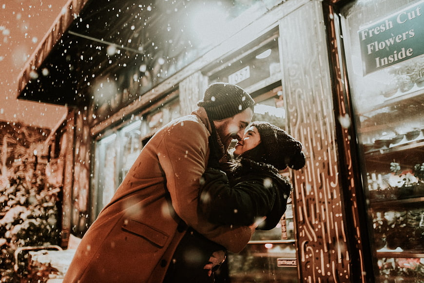 Romantic couple hugging in snow outside flower shop