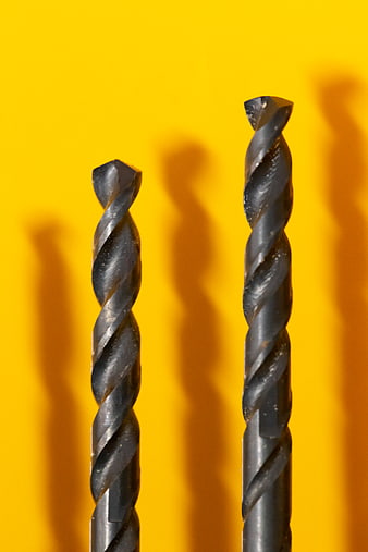 Close-up of two metal drill bits on yellow background