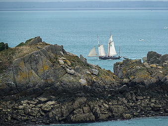Sailboat navigating rocky coastal landscape in Brittany