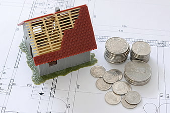 House model under construction with coins on architectural blueprint