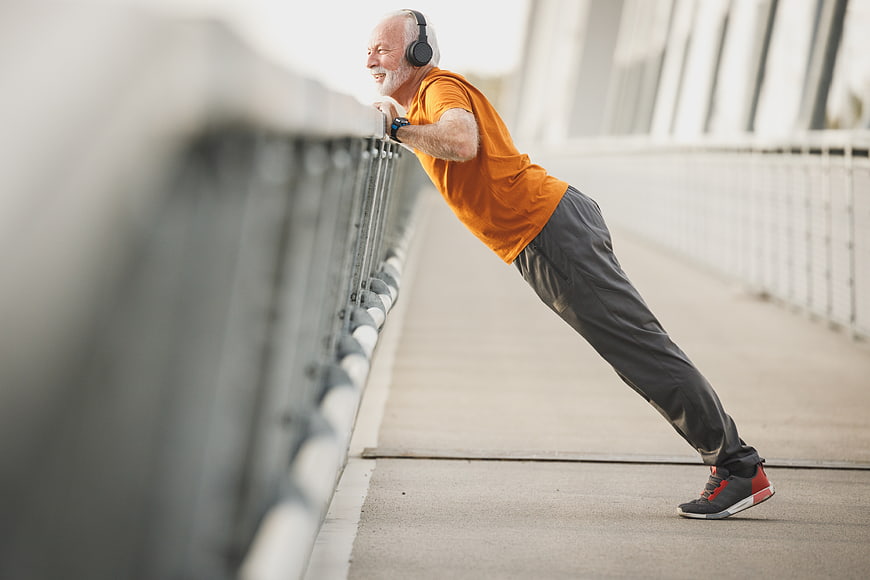 Senior man doing pushups on bridge railing with headphones