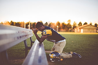 Football player kneeling in prayer on field bench