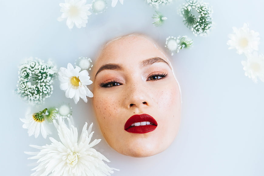 Woman's face submerged in milky water with white flowers