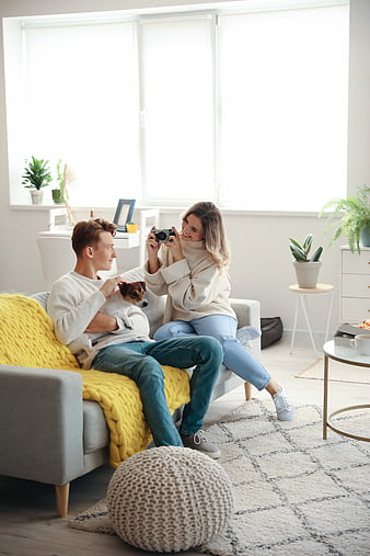 Happy couple taking photo with dog on sofa in bright living room