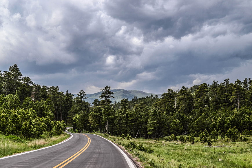 Winding Country Road Through Forest Under Dramatic Clouds