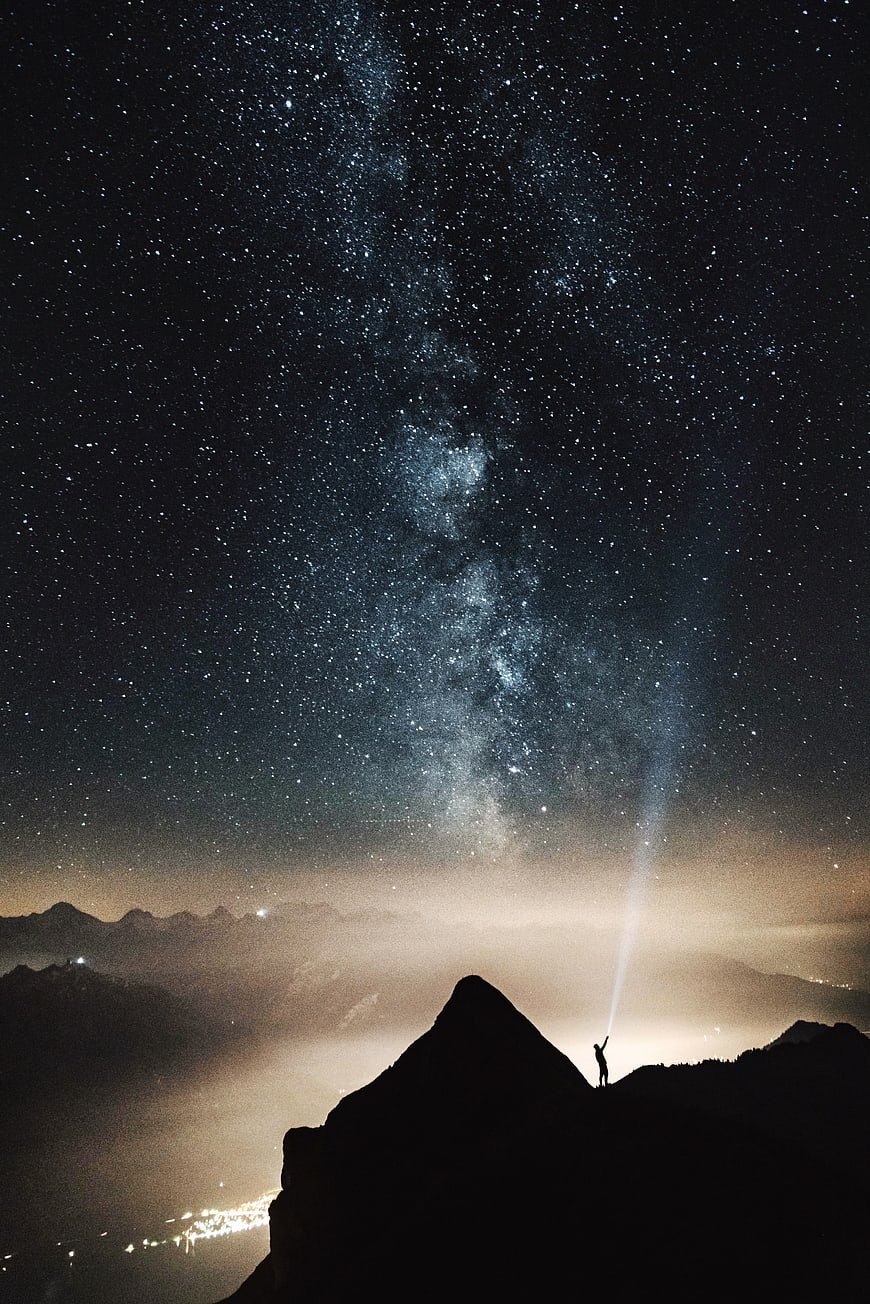 Silhouette of Person with Flashlight Under Milky Way