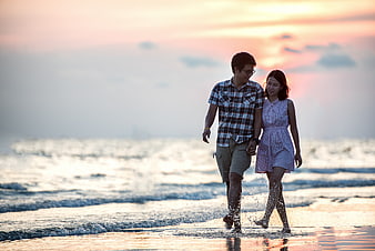Happy Asian Couple Walking Hand in Hand on Beach at Sunset