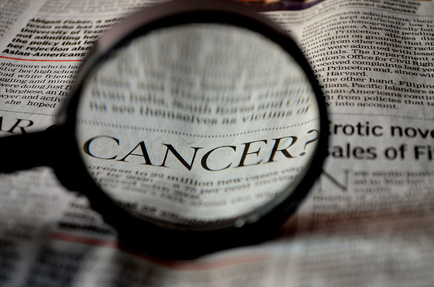 Magnifying glass focusing on the word cancer in a newspaper