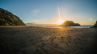 Sunset over sandy beach with footprints and coastal hills