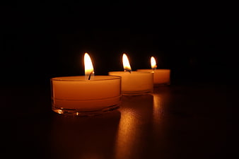 Three lit tea light candles in a row on dark background