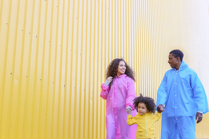 Happy Family in Colorful Raincoats Walking Past Yellow Wall