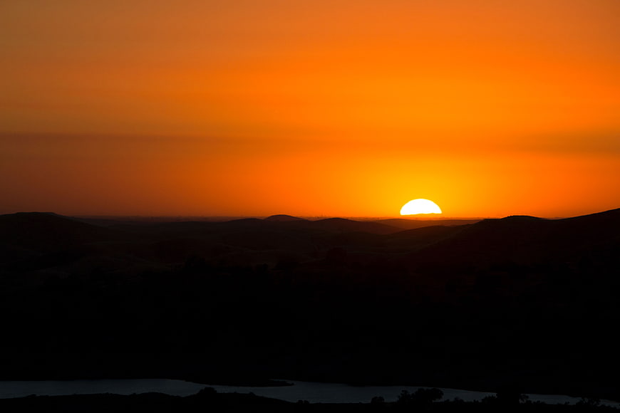 Vibrant Orange Sunset Over Silhouetted Rolling Hills Landscape