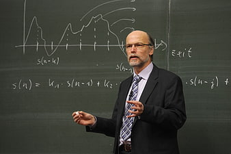 Senior male professor teaching physics in front of a green chalkboard