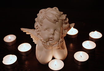 White angel figurine surrounded by lit tea light candles