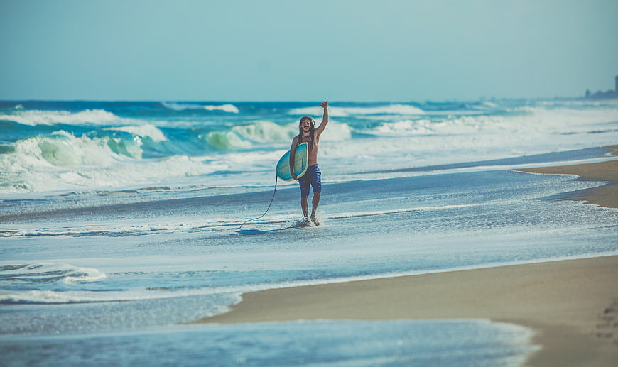Happy Surfer Walking on Beach with Board