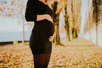 Pregnant woman holding belly in autumn park