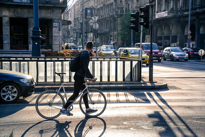 Man walking bicycle across city street intersection