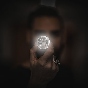 Man holding glowing moon orb in dark mysterious atmosphere