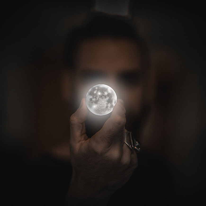 Man holding glowing moon orb in dark mysterious atmosphere