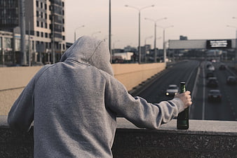 Lonely man in hoodie holding beer bottle overlooking highway