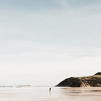 Lone Surfer Walking on Sandy Beach with Ocean and Hills