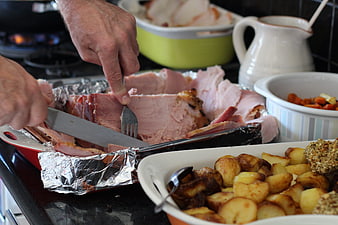 Hands Slicing Roast Ham With Roasted Potatoes And Holiday Sides