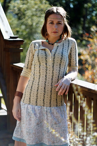 Young woman in boho dress standing on wooden deck outdoors