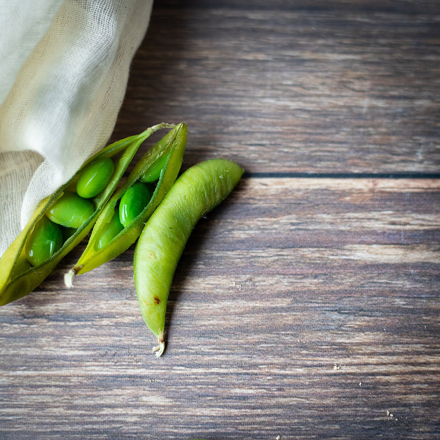 Fresh green peas spilling from linen bag on rustic wood