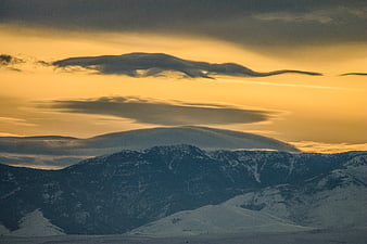 Dramatic sunset over snow-covered mountain range with lenticular clouds