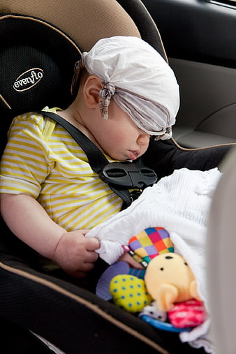 Sleeping baby in car seat with striped hat and toys
