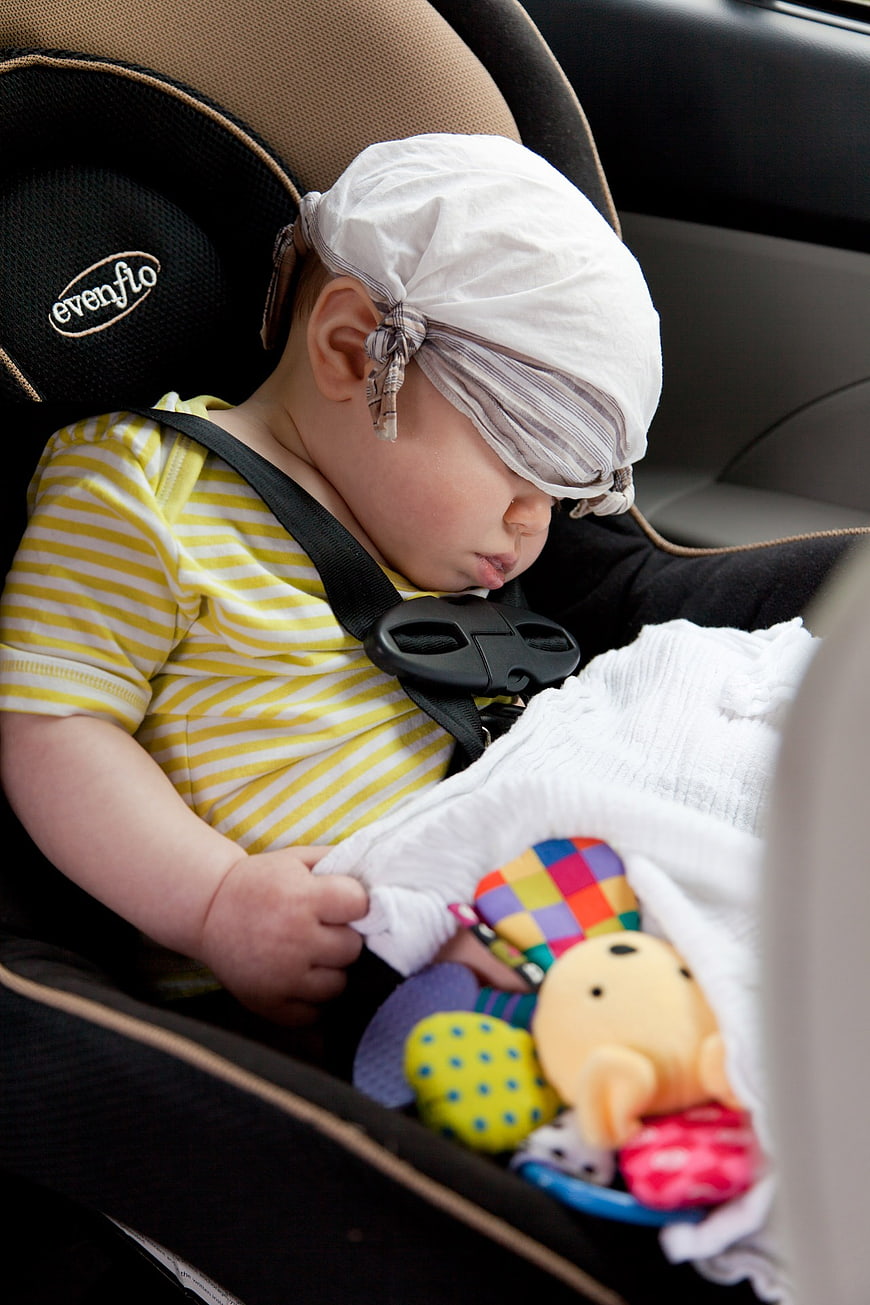 Sleeping baby in car seat with striped hat and toys