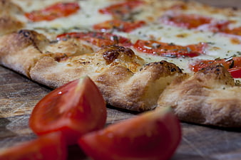 Close-up of rustic tomato pizza with fresh tomato wedges on wooden board