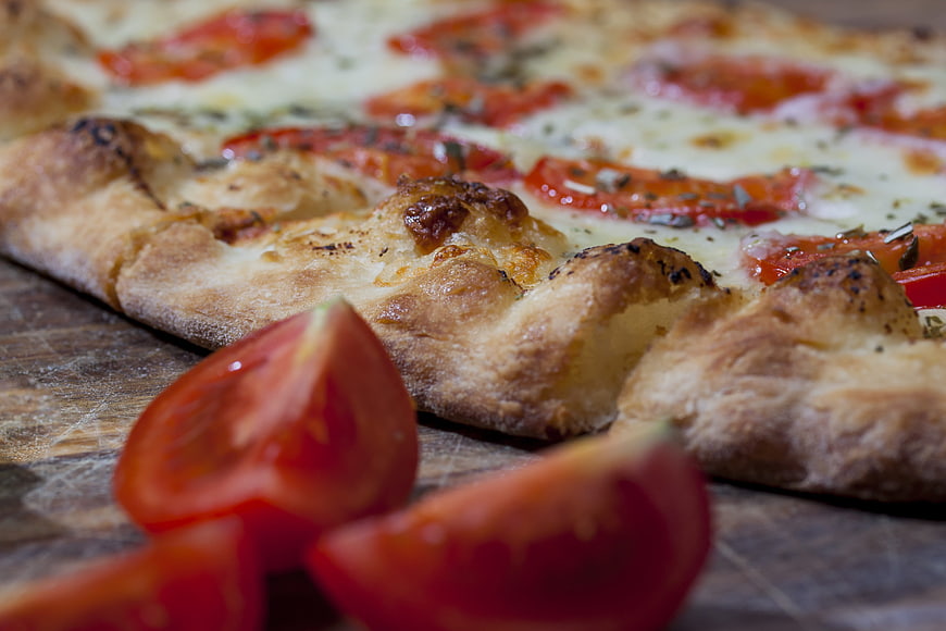 Close-up of rustic tomato pizza with fresh tomato wedges on wooden board
