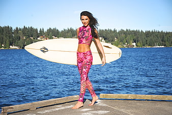 Woman with surfboard on dock by blue lake