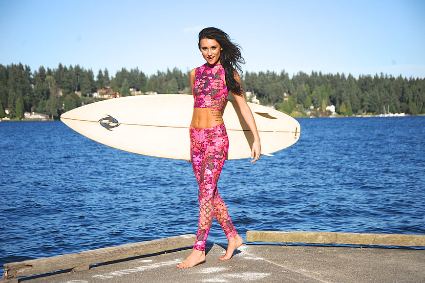 Woman with surfboard on dock by blue lake