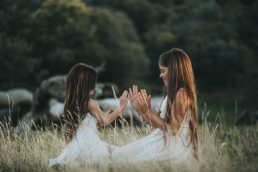 Two young girls playing hand clapping game in grassy field