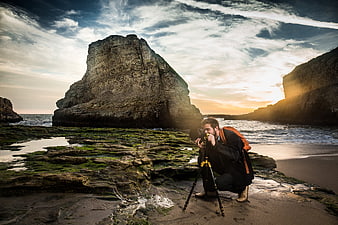 Photographer capturing sunset landscape on rocky coastal shore