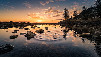 Serene Sunset Reflection on Rocky Shoreline with Ripples