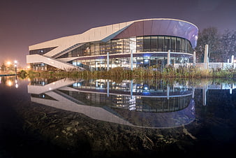 Modern curved building with glass facade reflected in water at night