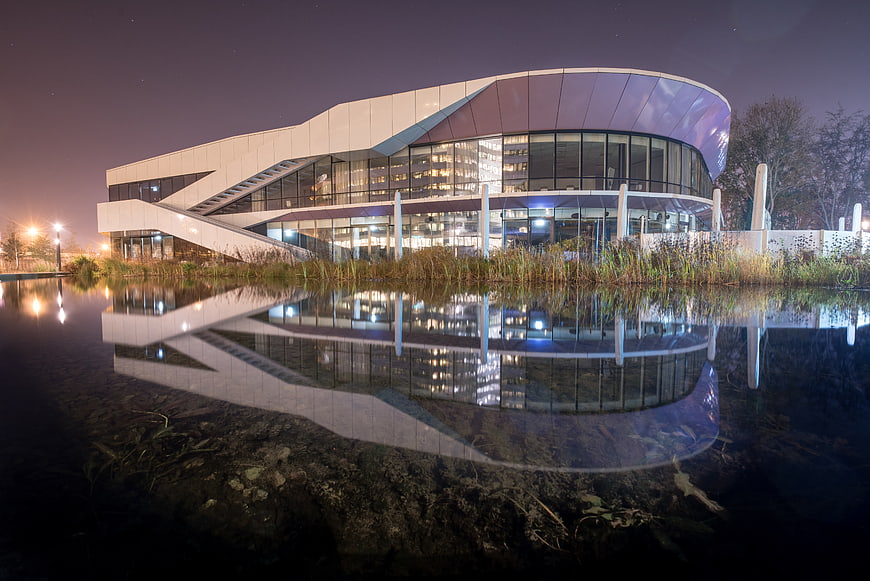 Modern curved building with glass facade reflected in water at night