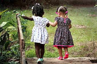 Two young girls holding hands walking away on wooden bridge