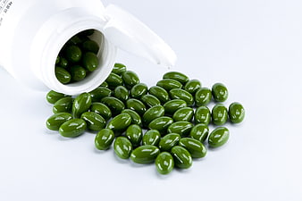 Green Health Supplements Spilling From White Bottle On White Background